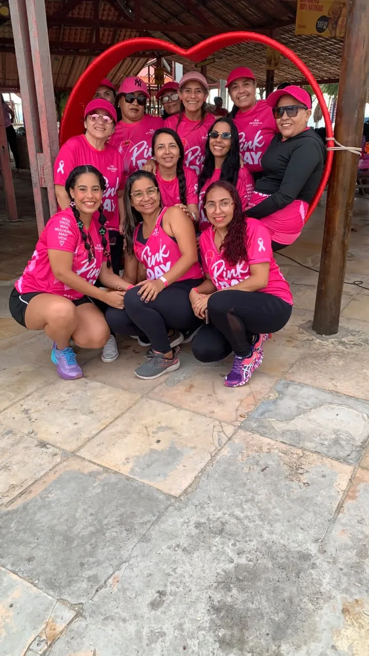 Grupo de mulheres com camisetas rosa do Pink Day posando diante de uma moldura vermelha em forma de coração.