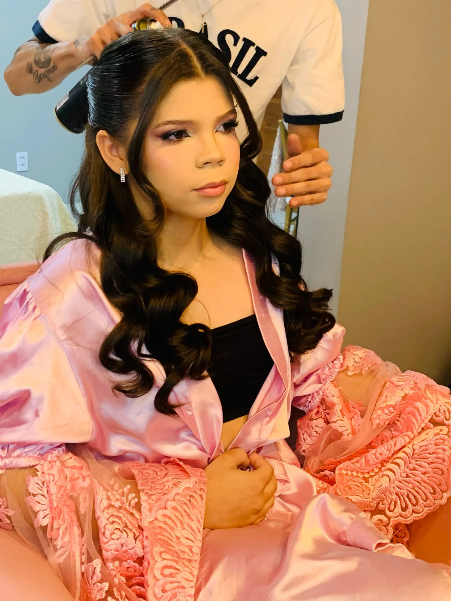 Cabeleireiro aplicando spray no penteado de uma jovem de roupão rosa.