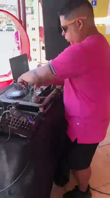 DJ de camisa rosa e óculos escuros mixando em uma controladora durante o evento.